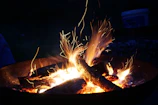 A close-up of a campfire crackling with glowing embers under a starry night sky