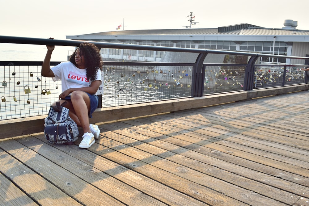 woman in white t-shirt sitting on black chair on brown wooden dock during daytime