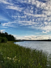 A quiet lakeside land plot with green grass and a clear blue water view, under a soft morning sky.