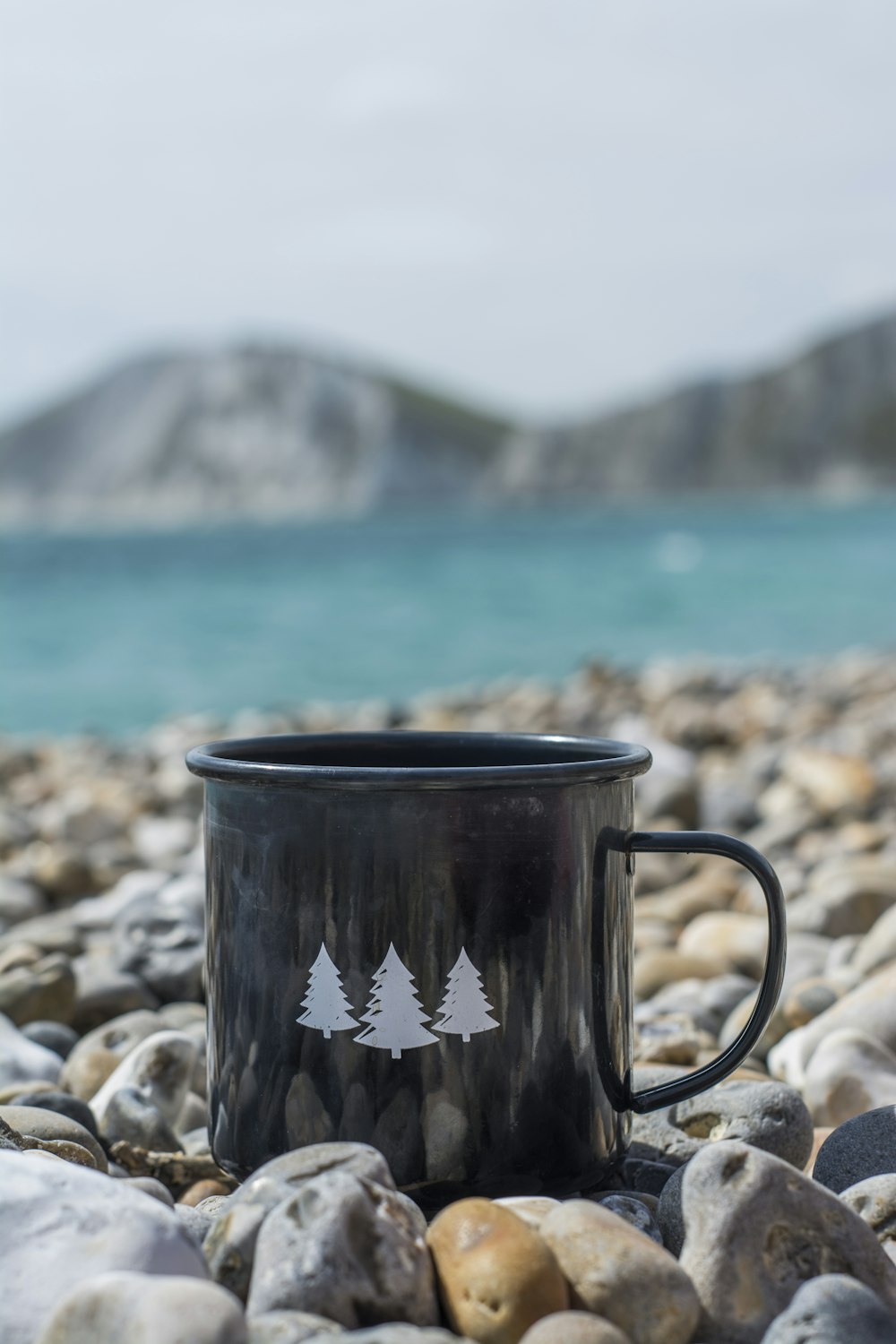 caneca de cerâmica preta e branca na costa rochosa durante o dia