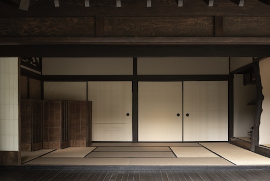 A traditional Japanese room featuring tatami mats, sliding shoji doors, and wooden elements. The interior is minimalistic, with a focus on simplicity and natural materials, creating a harmonious and serene atmosphere.