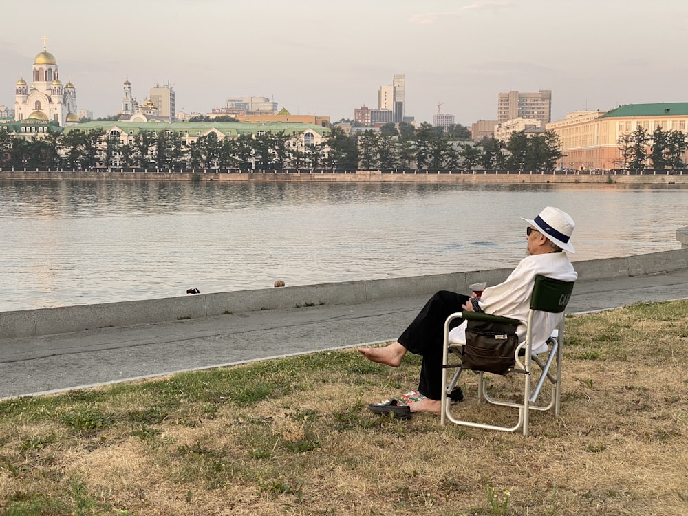 man in black shirt and white cap sitting on chair near body of water during daytime