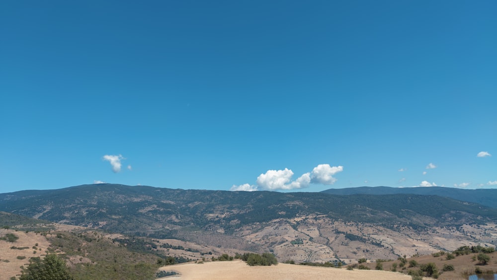 green grass field and mountains under blue sky during daytime