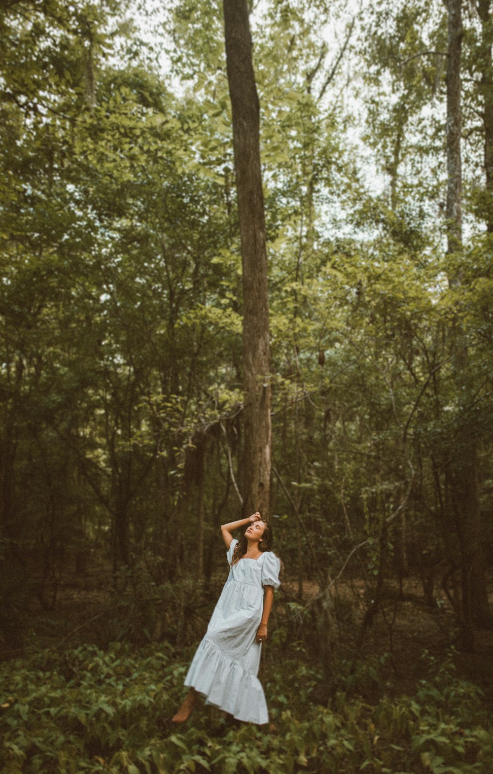 woman in white dress standing in the middle of the forest during daytime