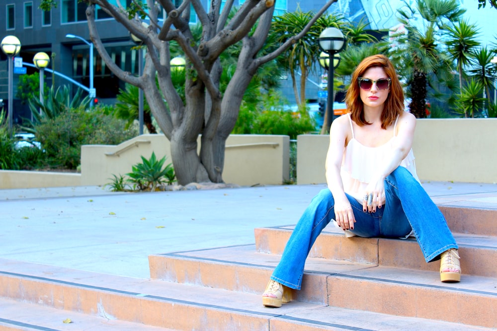 woman in white long sleeve shirt and blue denim jeans sitting on brown concrete bench during