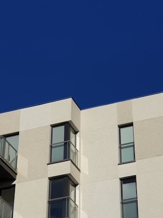 A modern home facade featuring large glass curtain walls with minimal framing under a clear blue sky.