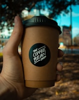 Hands holding a lattidos drip coffee pack with a blurred coffee farm background.