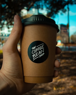 Hands holding a lattidos drip coffee pack with a blurred coffee farm background.