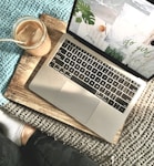 macbook pro beside white ceramic mug on brown wooden table