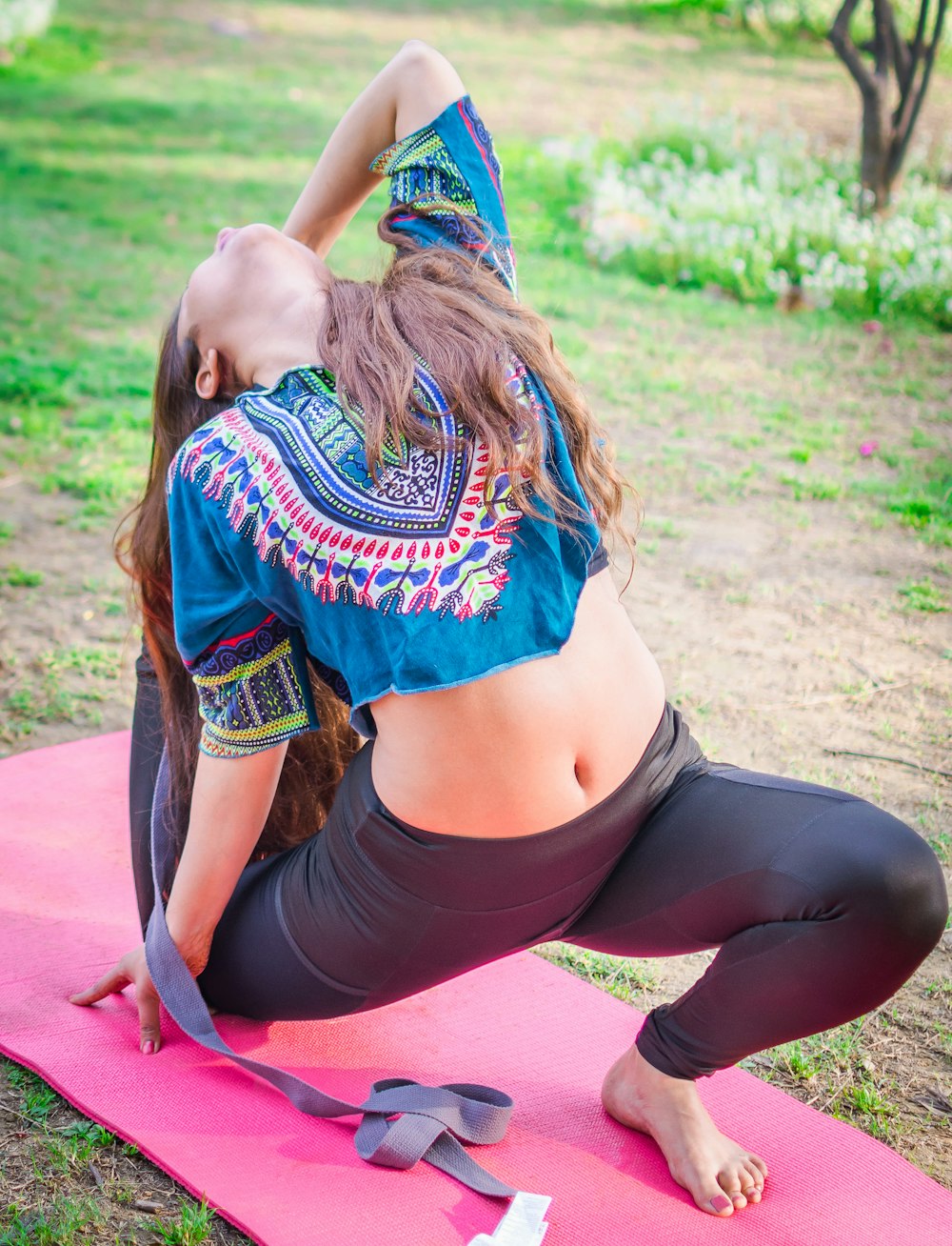 woman in black leggings and green and red shirt sitting on pink mat