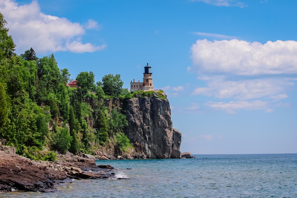 white and brown lighthouse on cliff beside body of water during daytime
