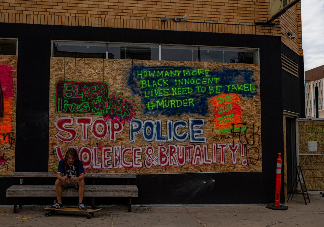 man in black t-shirt sitting on bench beside graffiti wall during daytime