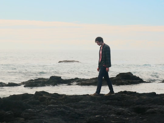 man in red jacket standing on black rock near sea during daytime in Narooma NSW Australia