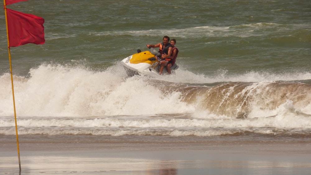 昼間、海の波に黄色と白のサーフボードに乗る黒いショートパンツの男