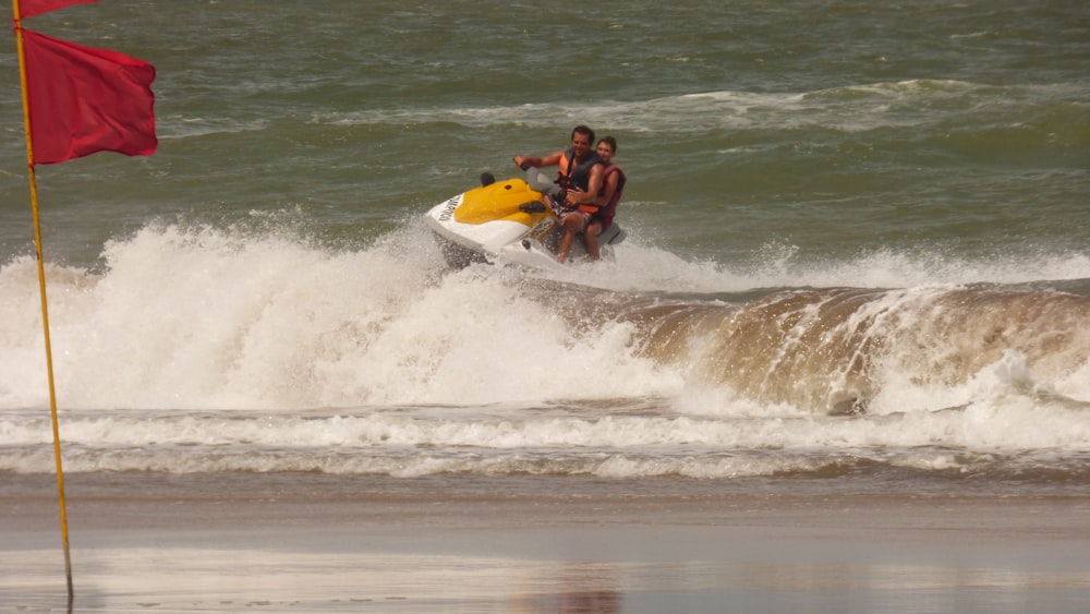 Uomo in pantaloncini neri che cavalca la tavola da surf gialla e bianca sulle onde del mare durante il giorno