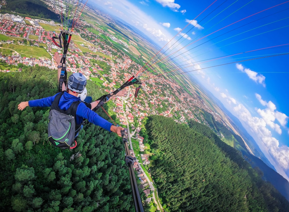 hombre con chaqueta azul y jeans de mezclilla azul montando en teleférico sobre árboles verdes durante