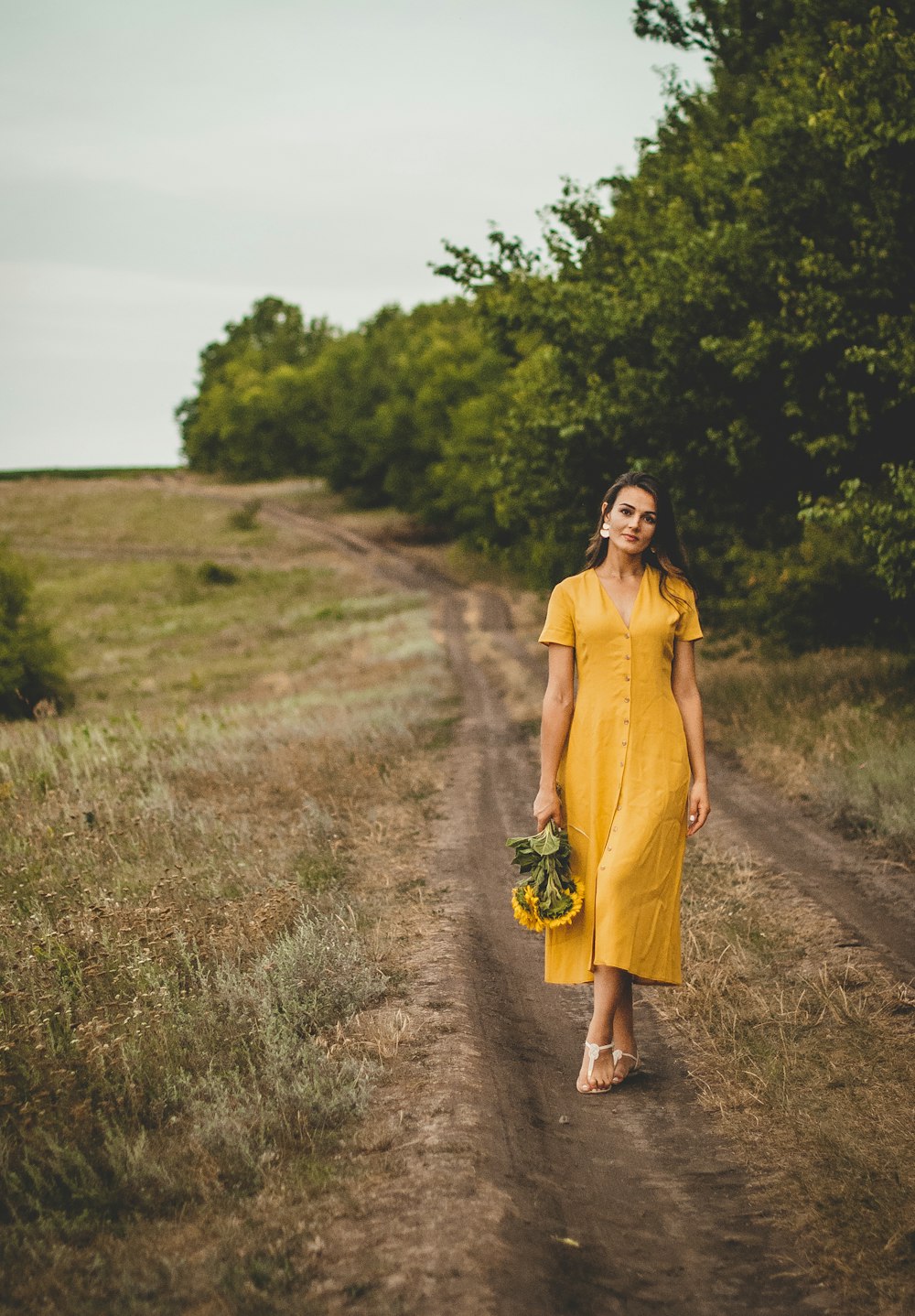 woman in yellow long sleeve dress standing on brown dirt road during daytime