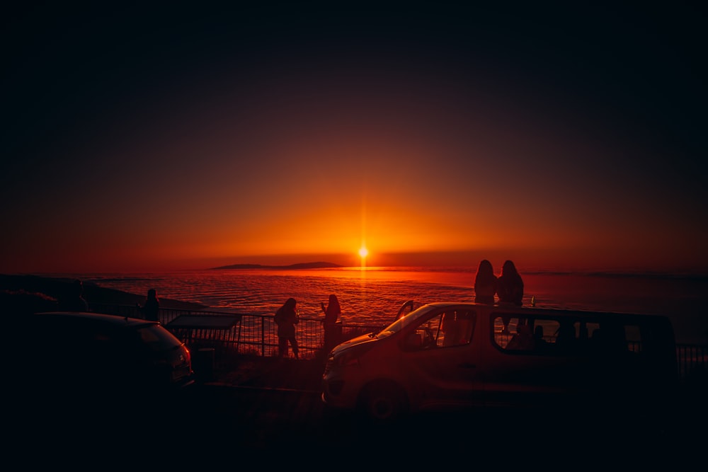 silhouette of people near body of water during sunset