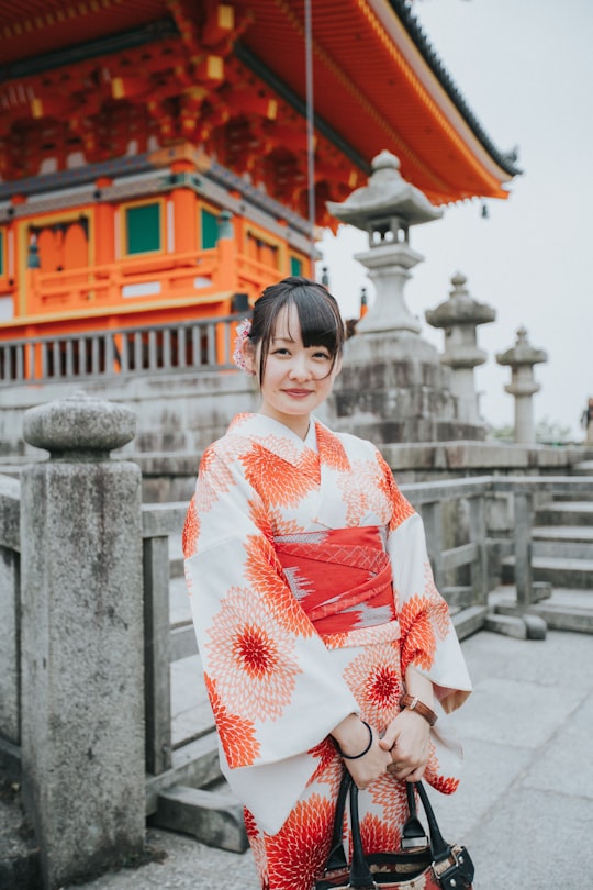 woman in white and red kimono standing near white concrete building during daytime in Kiyomizu-dera Japan