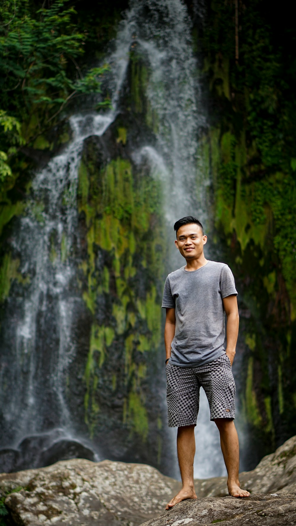homem em camiseta cinza pescoço da tripulação em pé perto de cachoeiras durante o dia