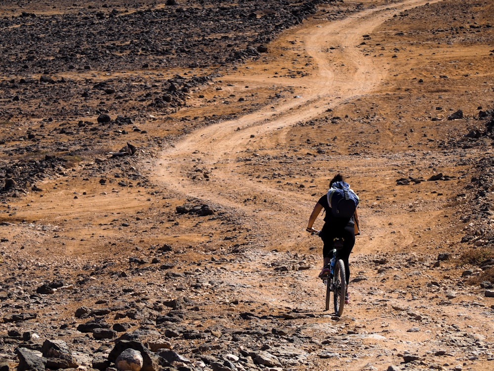 낮 동안 갈색 모래 위에서 자전거를 타는 검은 재킷을 입은 남자