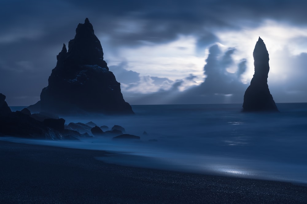 白い雲の下の海に浮かぶ黒い岩層