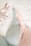 A close-up view of two delicate lace bras, one in soft green and the other in light pink, lying on a white surface. Beside them is a small branch with cotton flowers, adding a natural and cozy element to the composition.