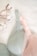 A close-up view of two delicate lace bras, one in soft green and the other in light pink, lying on a white surface. Beside them is a small branch with cotton flowers, adding a natural and cozy element to the composition.