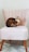 A Bengal cat with striking markings is seated on a plush, pale pink chair with wooden legs. The setting appears to be indoors, with a wooden floor and a geometric-patterned rug partially visible beneath the chair.