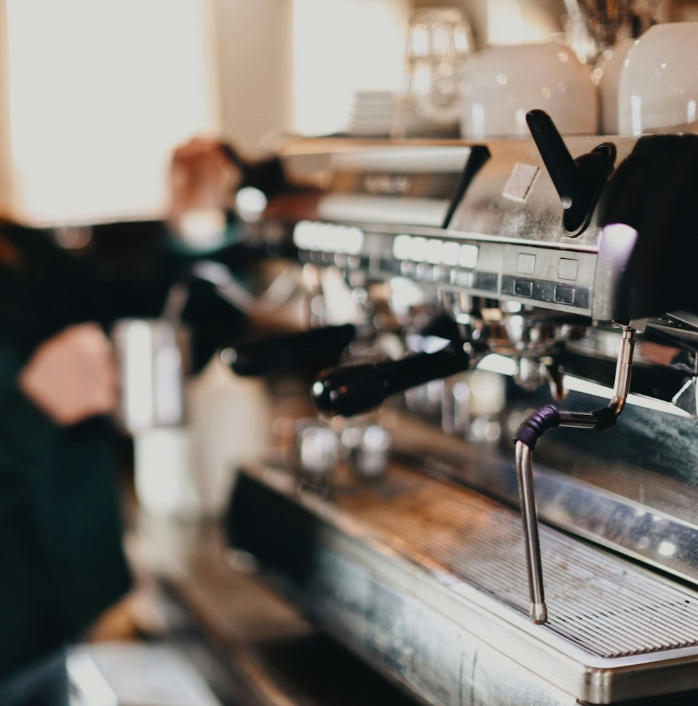 Person in schwarzem Hemd und schwarzer Hose vor der Espressomaschine