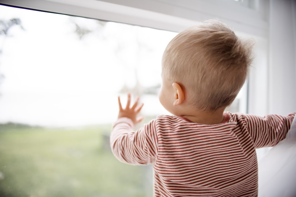 赤と白の縞模様のシャツを着た子供が窓の外を眺めている