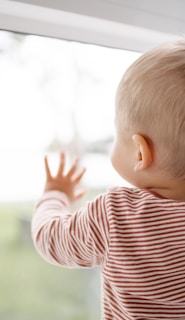 child in red and white striped shirt looking out the window