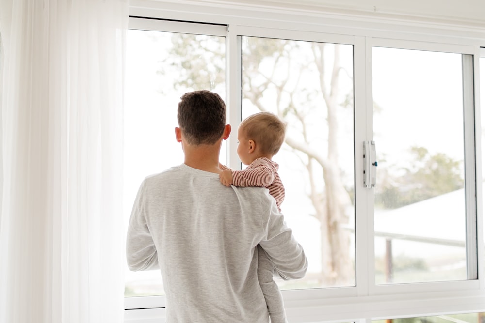 Junge im grauen Pullover steht tagsüber am Fenster