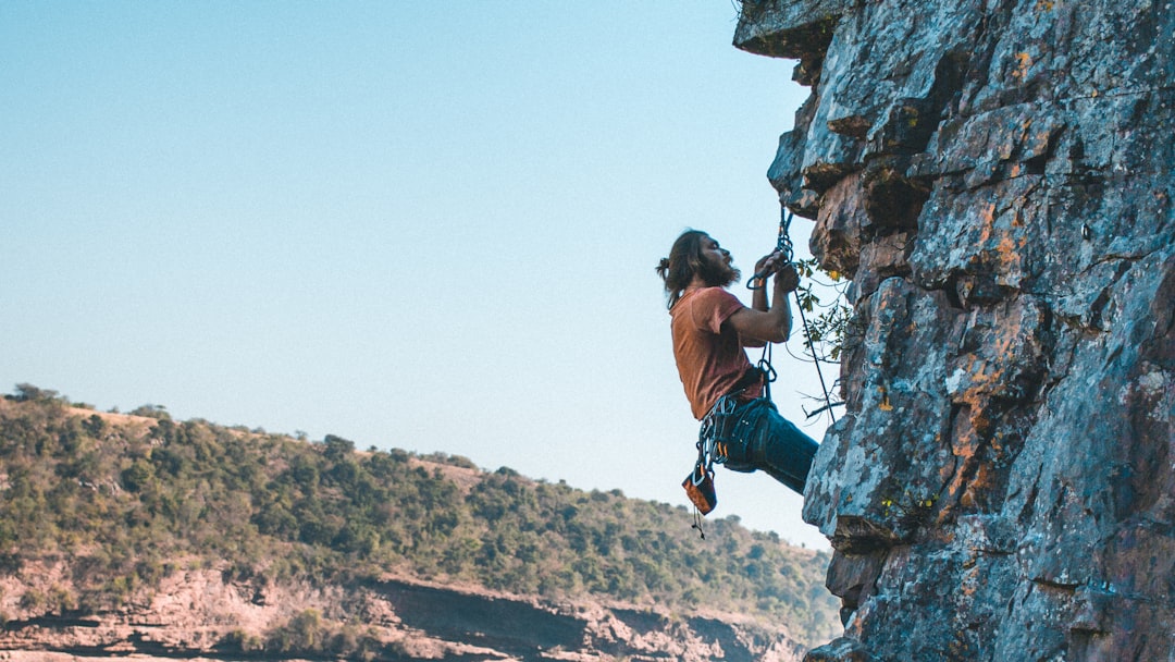 man in blue tank top and brown shorts climbing on rocky mountain during daytime