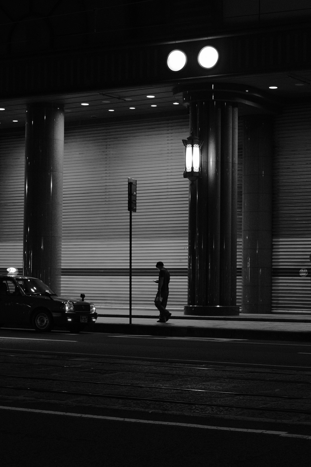 grayscale photo of man standing beside car