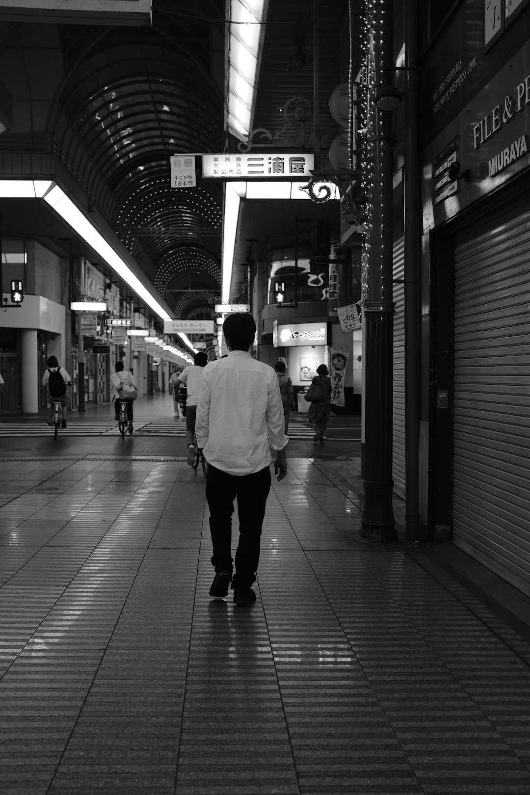 grayscale photo of man in white long sleeve shirt walking on train station