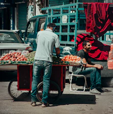 A vendor arranging fresh fruits on a colorful street market cart during morning hours.