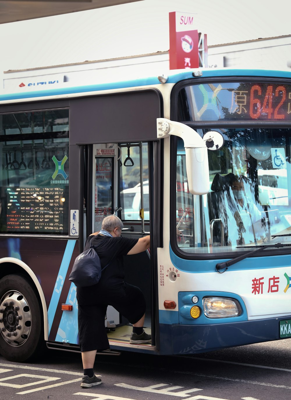 man in black jacket and blue denim jeans standing beside white and blue bus during daytime