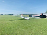 A glider pilot preparing the plane on a sunny airfield with mountains in the background.