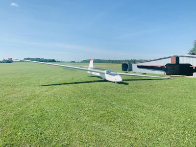 A glider pilot preparing the plane on a sunny airfield with mountains in the background.