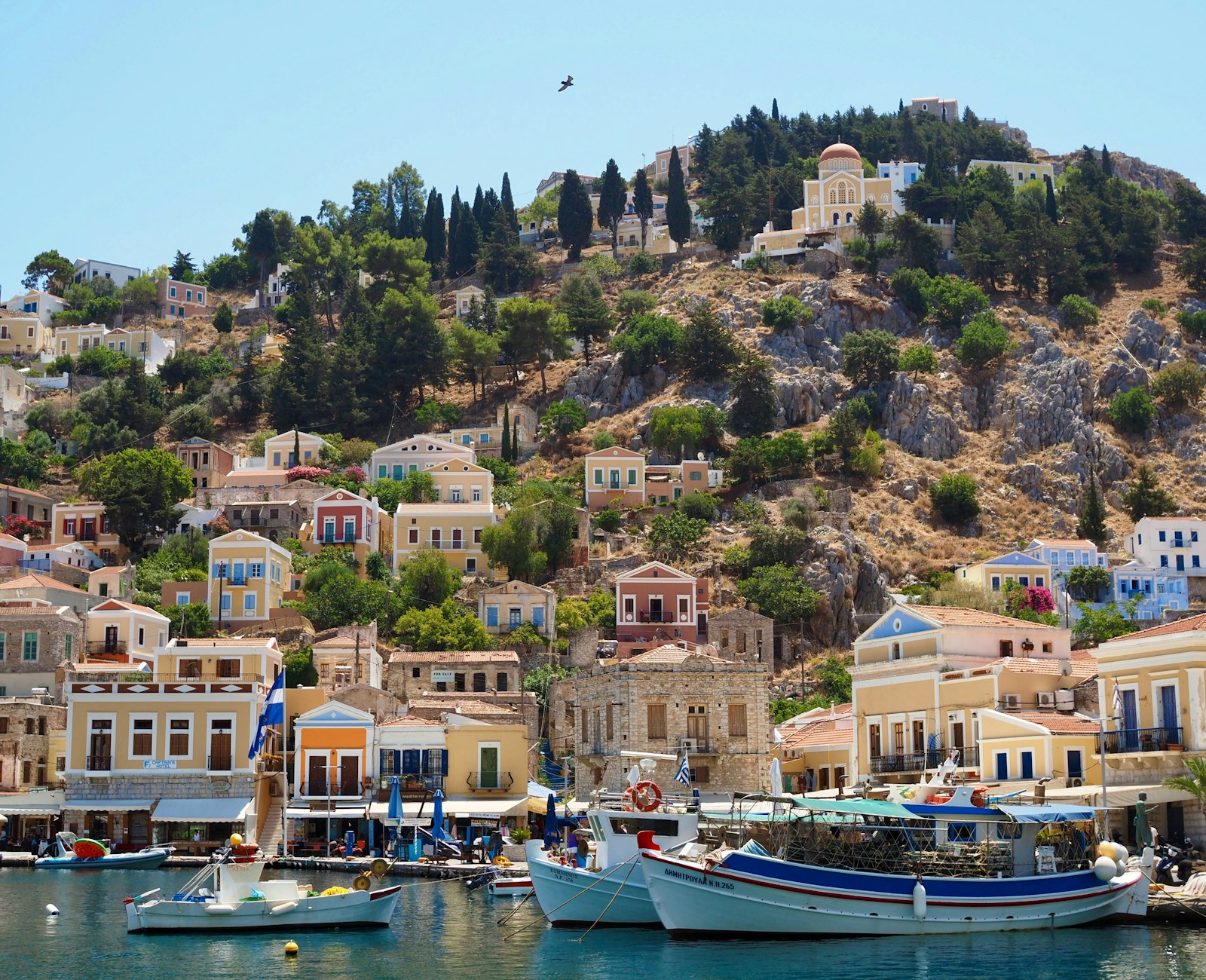 Pastel neoclassical houses climbing the hillside above the harbor of Symi