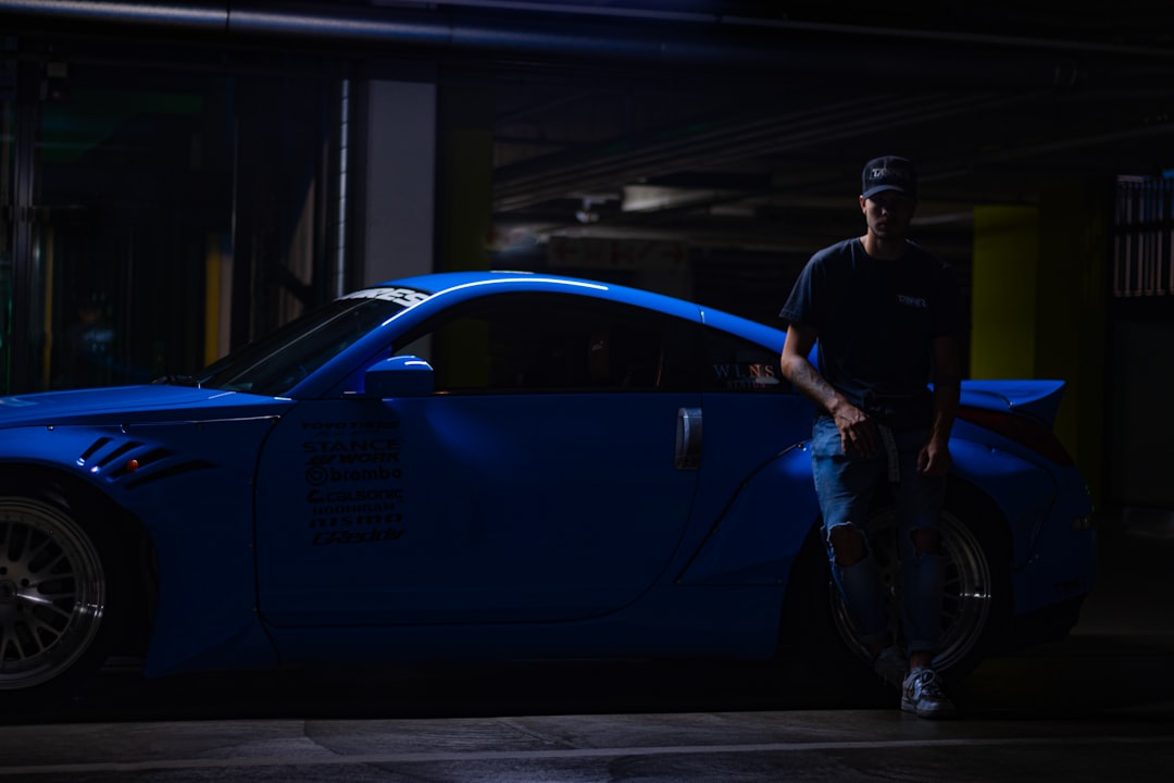 man in black t-shirt and black pants standing beside blue car during daytime