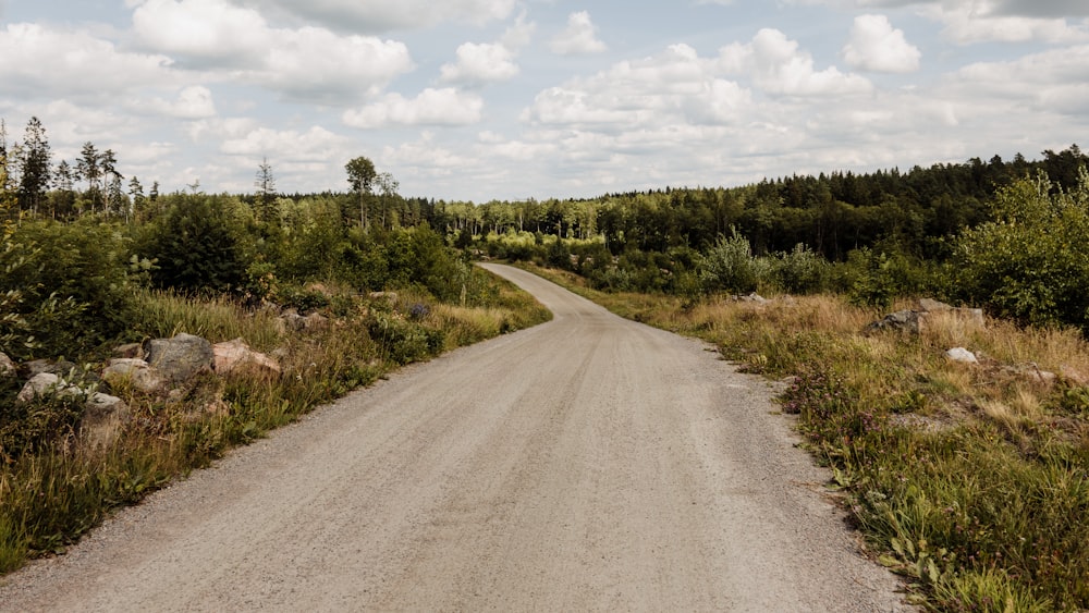 gray asphalt road between green grass field under blue and white sunny cloudy sky during daytime