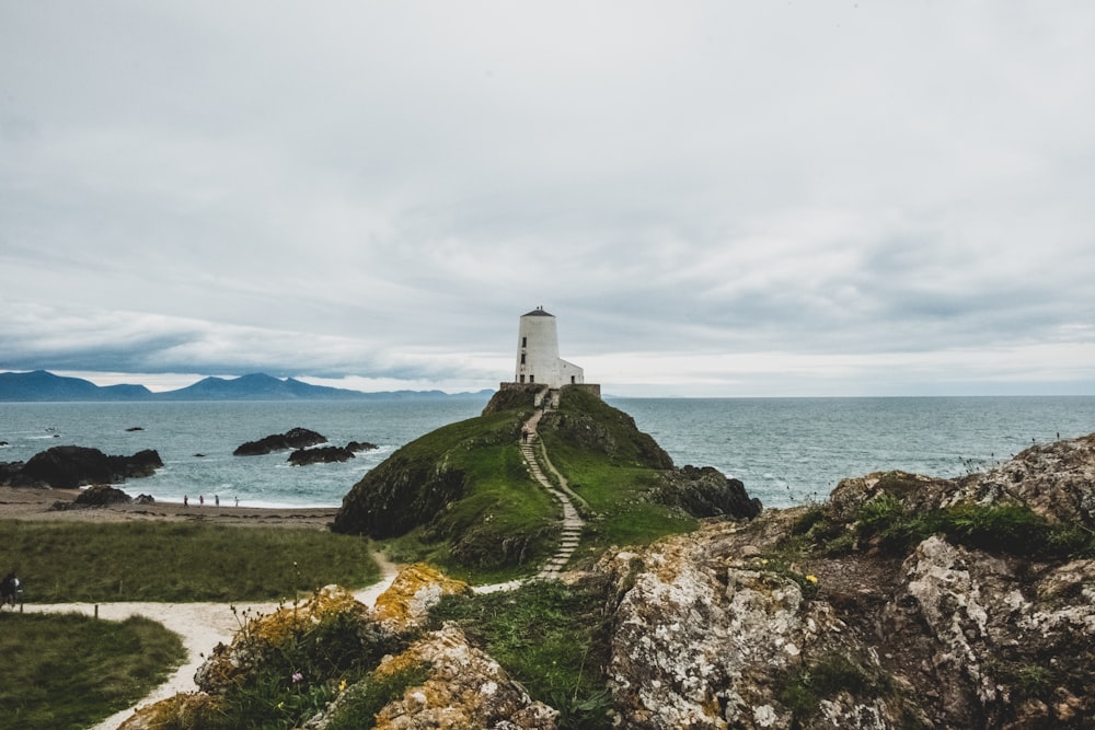 white lighthouse on green grass field near body of water during daytime