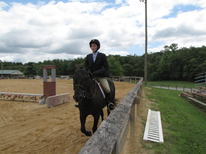 A skilled trainer guiding a student on horseback across a lush, open riding arena at Black Stallion Equestrian.