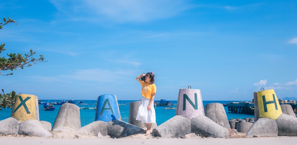 woman in white dress standing on gray rock near body of water during daytime