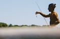 Angler holding a fishing rod with a bright, clear sky in the background.