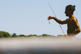 Angler holding a fishing rod with a bright, clear sky in the background.
