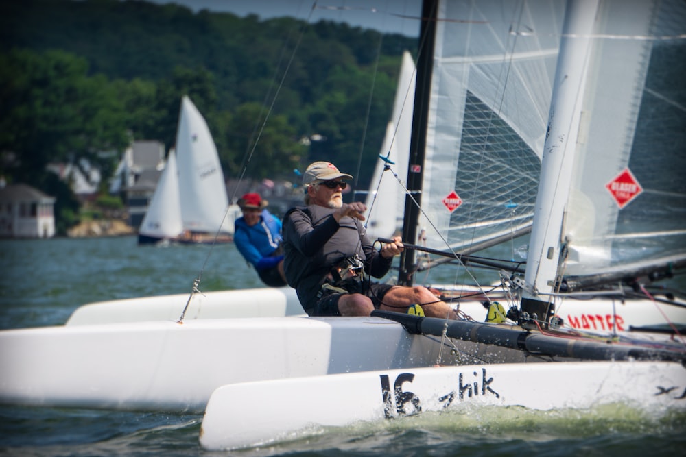 2 men in blue and black jacket riding on white sail boat during daytime