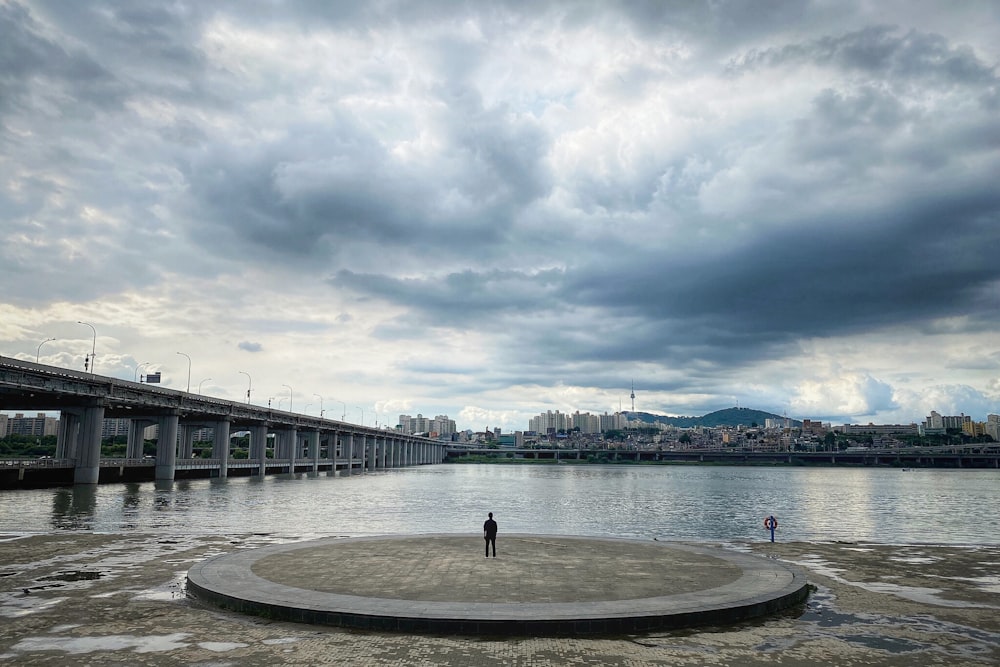 gray concrete bridge over body of water under cloudy sky during daytime